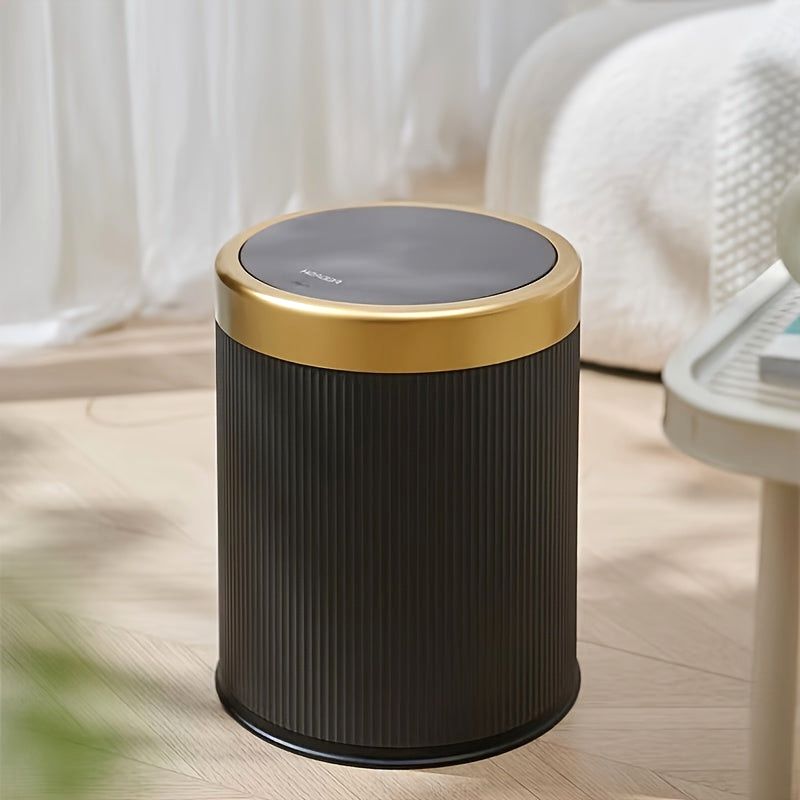 Black Elegance Oval Waste Solution trash can with a press-top lid and gold rim, placed in a modern bedroom setting next to a bed.