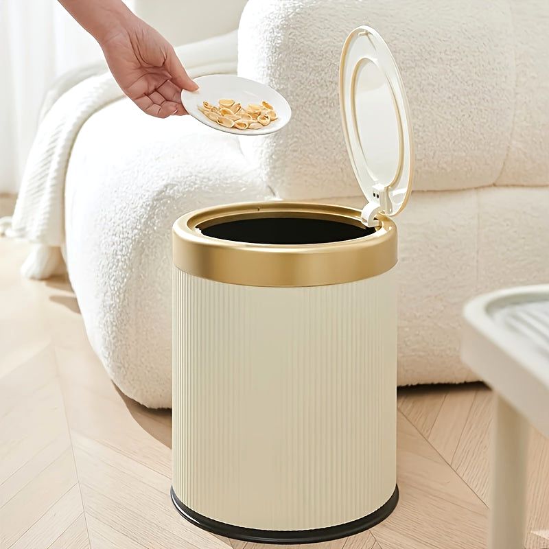 Cream Elegance Oval Waste Solution trash can with a press-top lid and gold rim, placed in a living room setting with a hand dropping food scraps from a plate into the open bin.