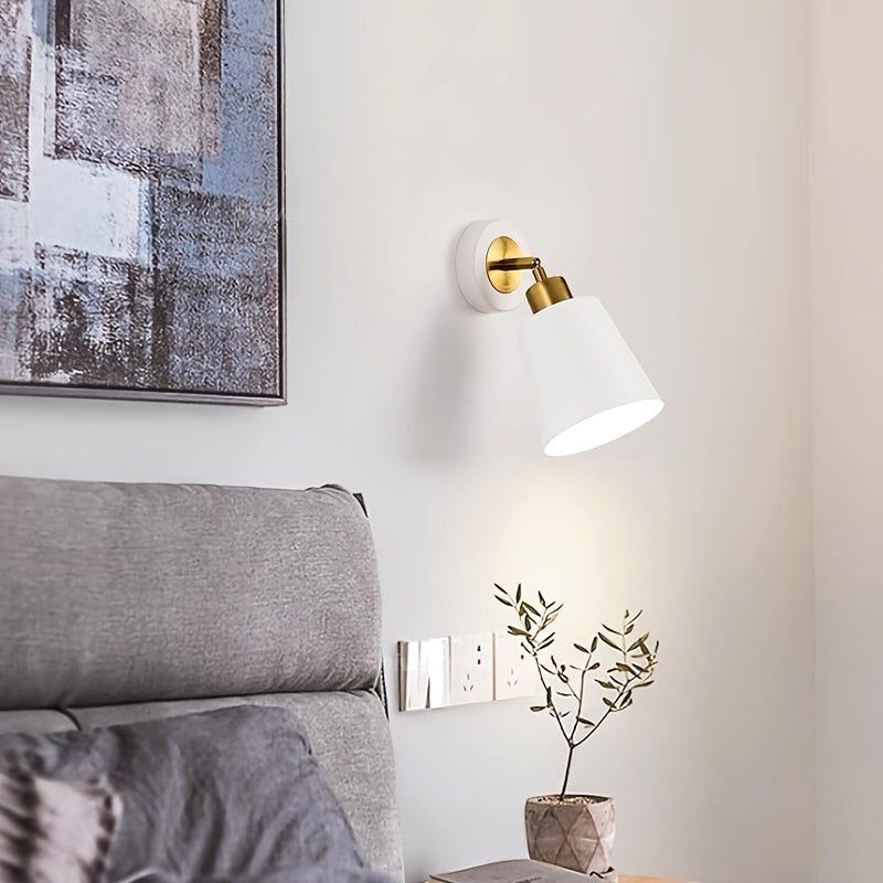 White Luna Glow adjustable wall sconce light with brushed metal finish, illuminating a bedside table with a plant and power outlets, next to a bed with a grey headboard and an abstract painting.